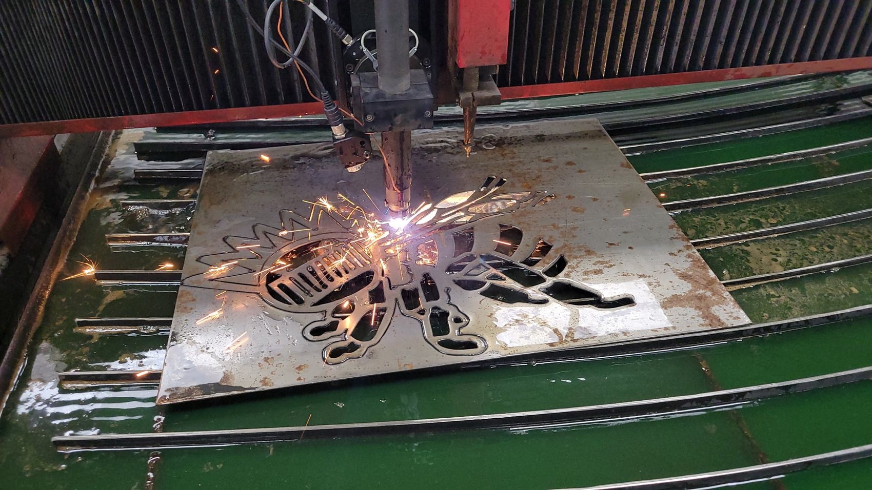 Close-up of the CNC plasma table cutting a detailed bee design into steel