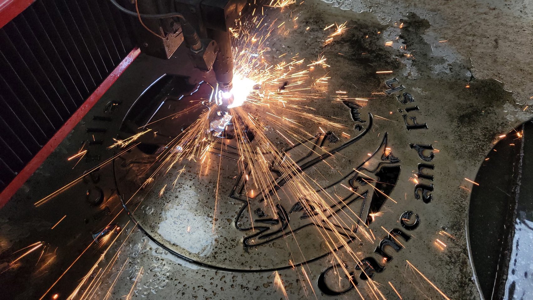 CNC plasma table cutting a custom Game and Fish emblem into steel plate with sparks flying