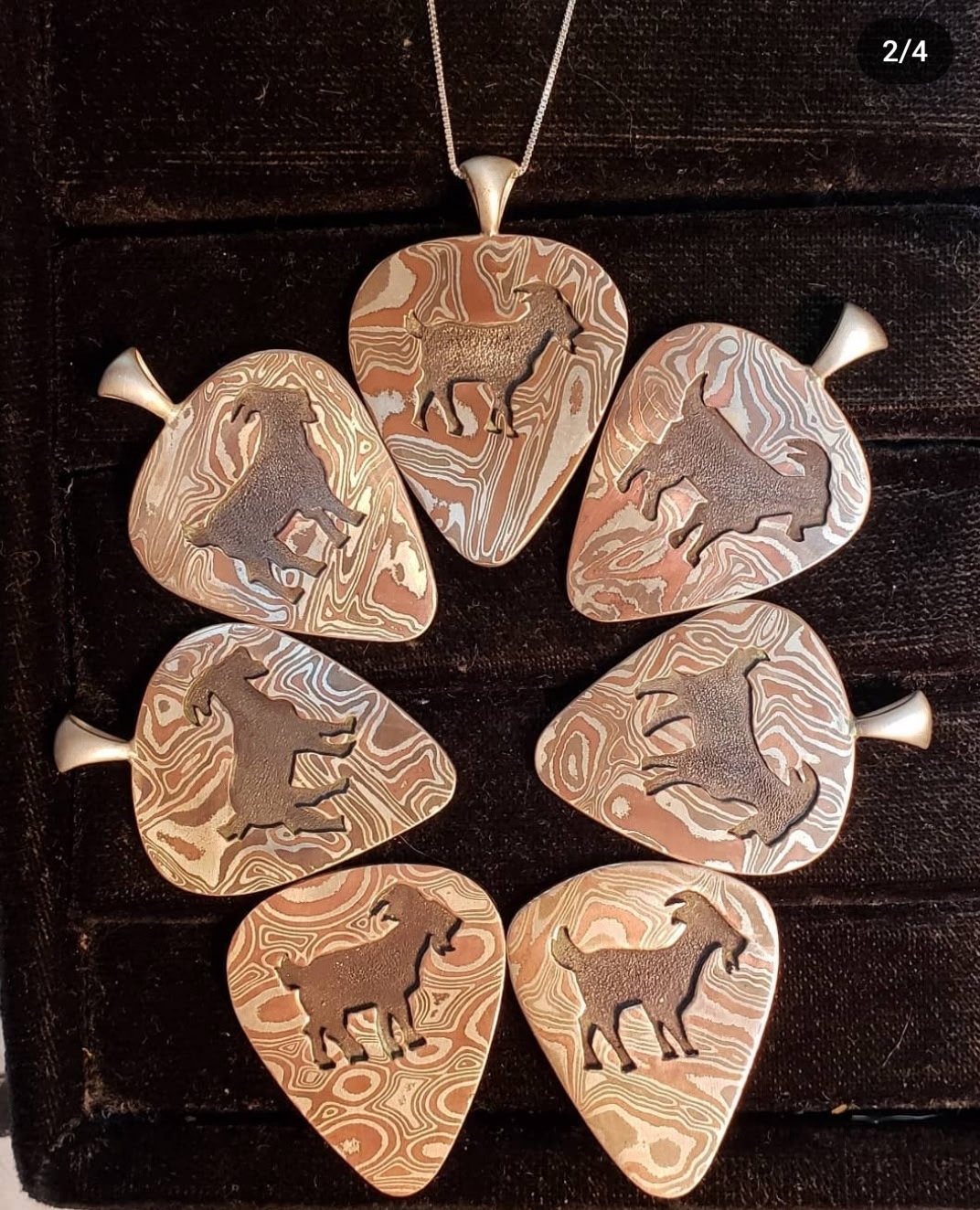 Seven mountain goat pendants cut from mokume gane metal arranged in a circle on sterling chains