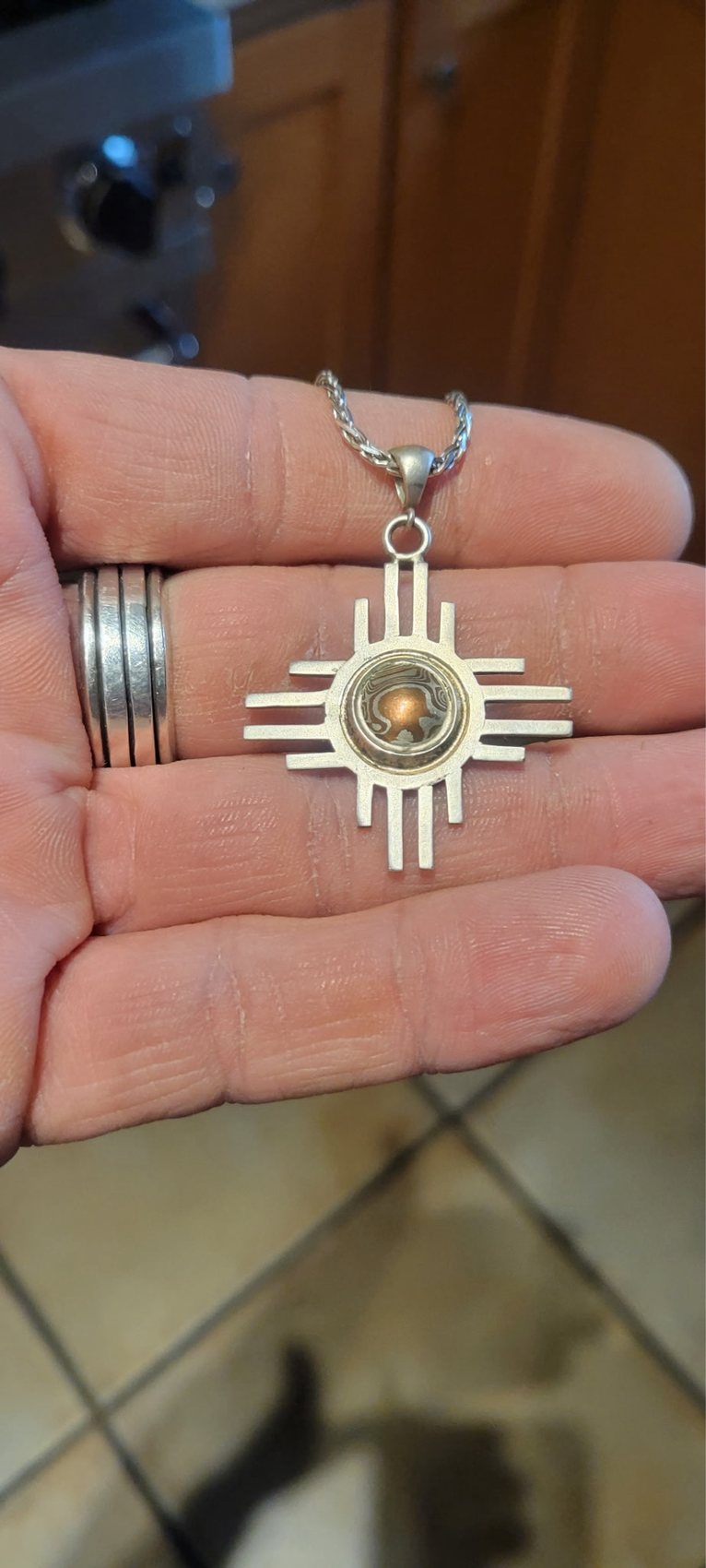 Sterling silver Zia sun pendant with a mokume gane center stone, held in hand alongside matching rings