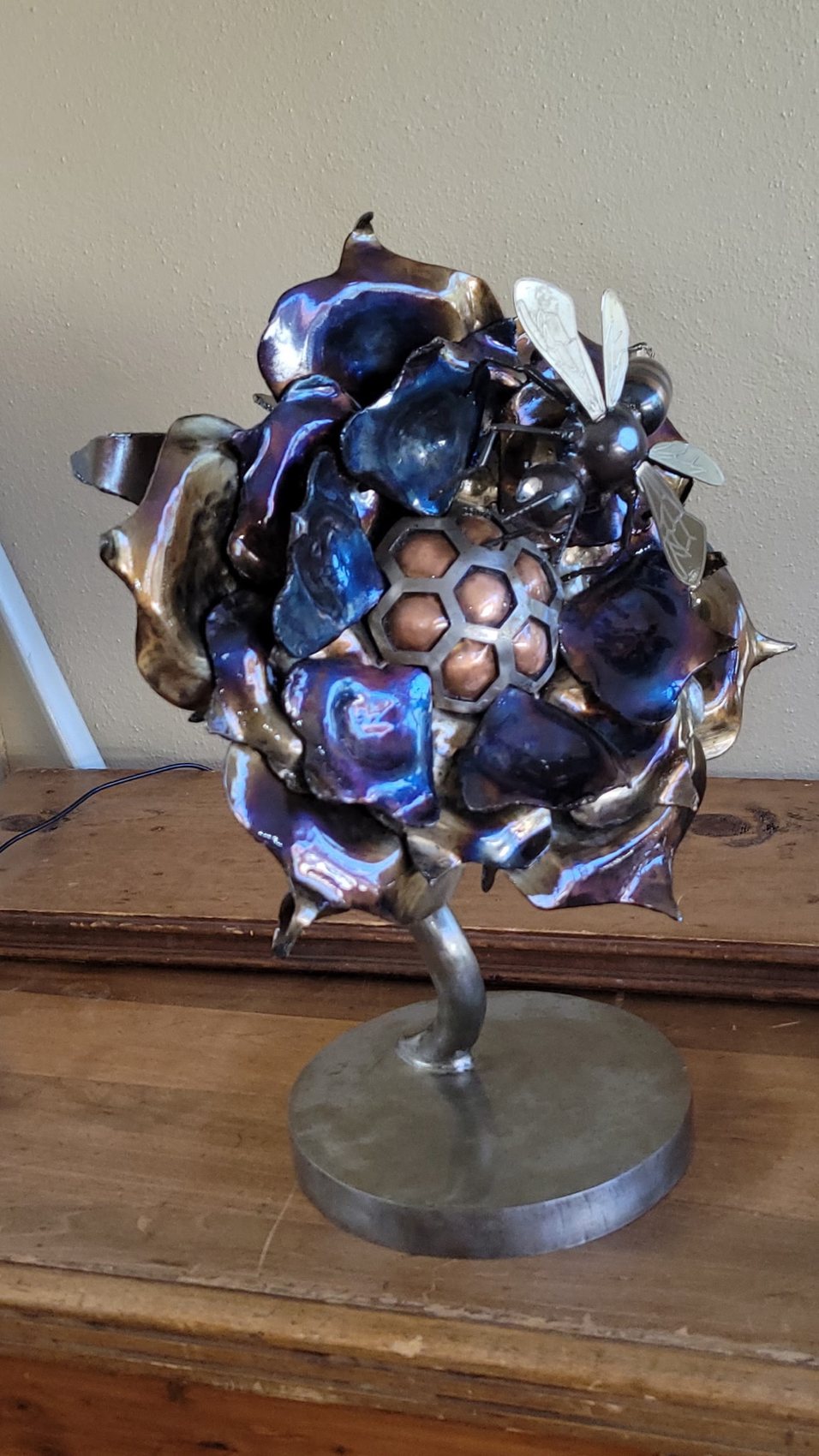 Torch-patina steel flower sculpture with bees resting on a honeycomb center, finished in blue and gold tones