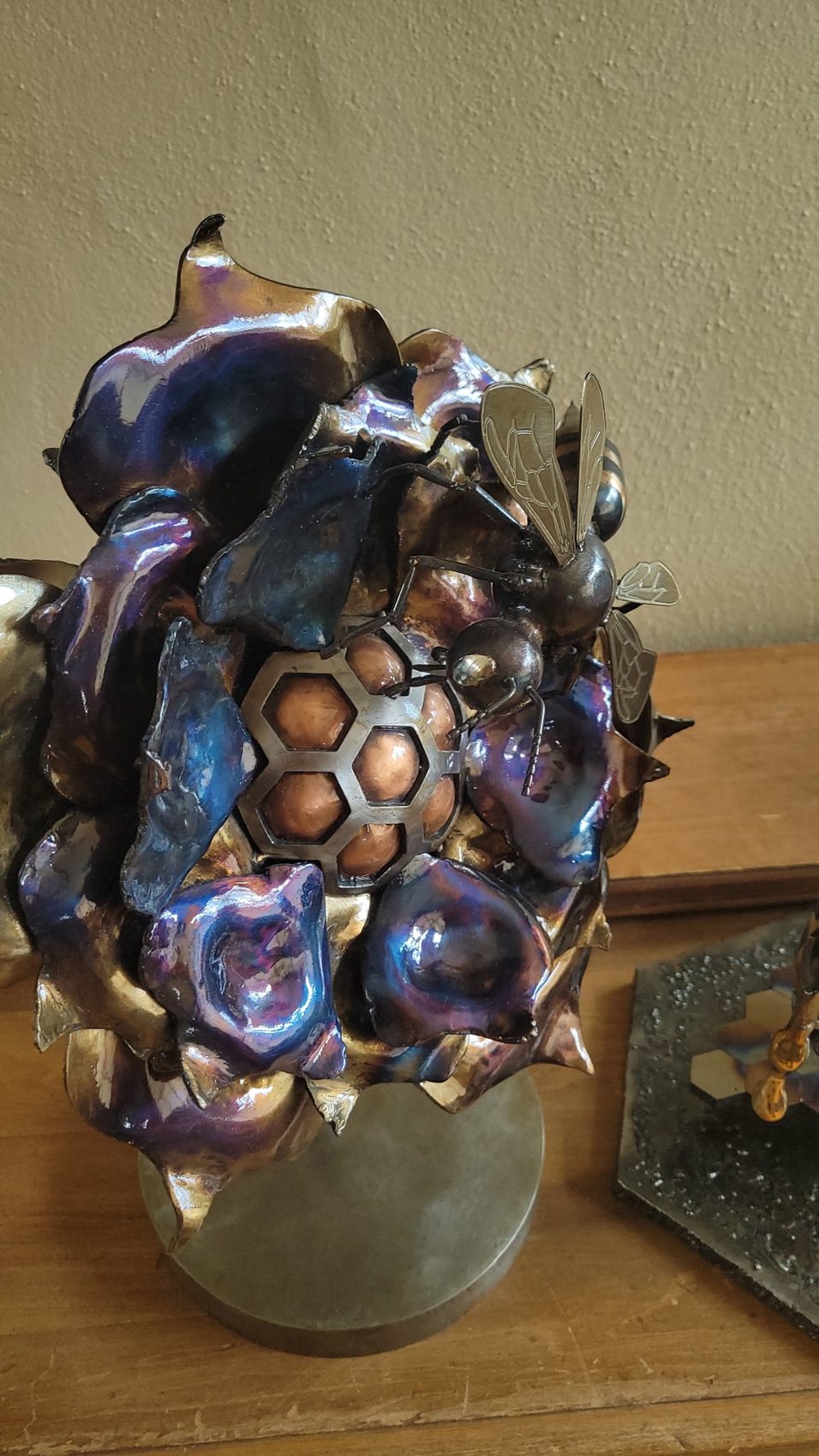 Detail view of the torch-patina steel flower sculpture showing the honeycomb center and bees