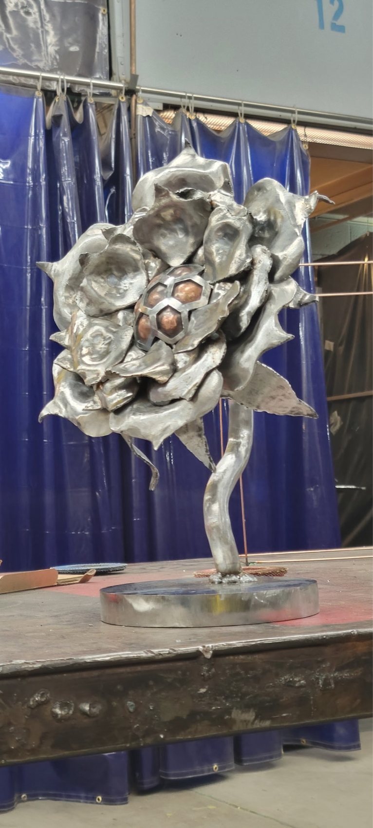Raw steel rose sculpture in progress on the welding table in the shop